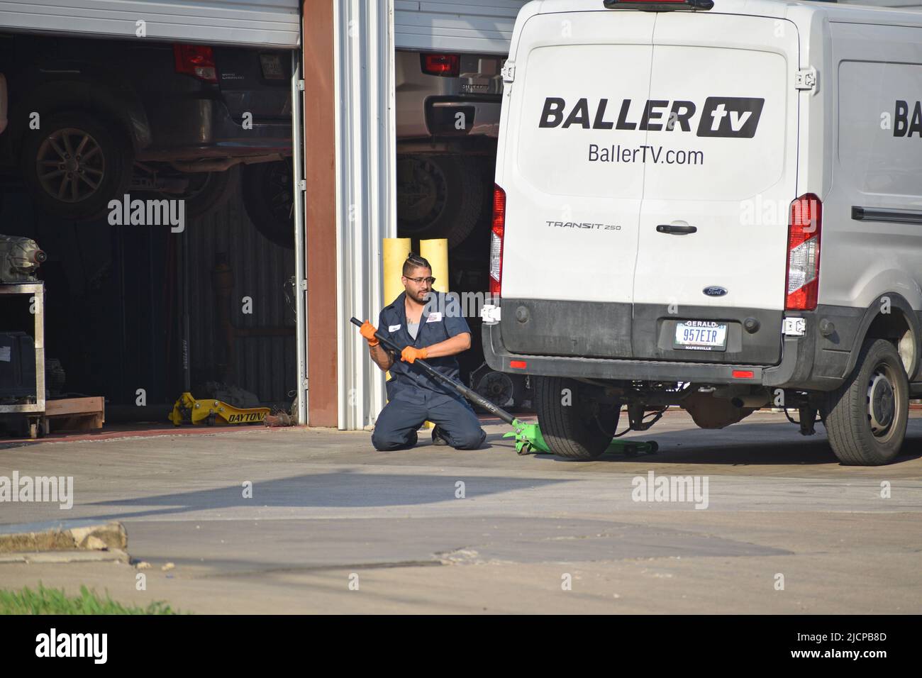 Un lavoratore di un'officina di pneumatici che utilizza un martinetto per sollevare un furgone da lavoro Foto Stock