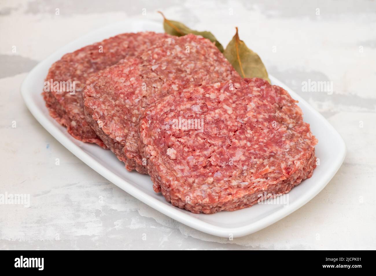 carni fresche macinate crude su piatto bianco con alloro Foto Stock