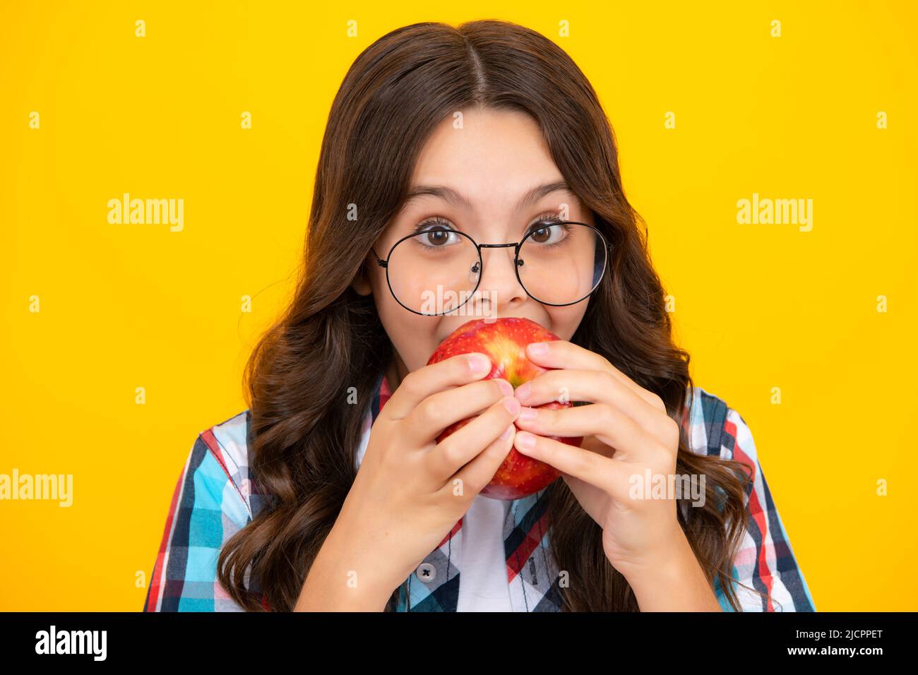 Bambina che mangia una mela sopra isolato sfondo giallo studio. Primo piano faccia di tennager con frutta. Ritratto di felice divertente sorridente bambino adolescente Foto Stock