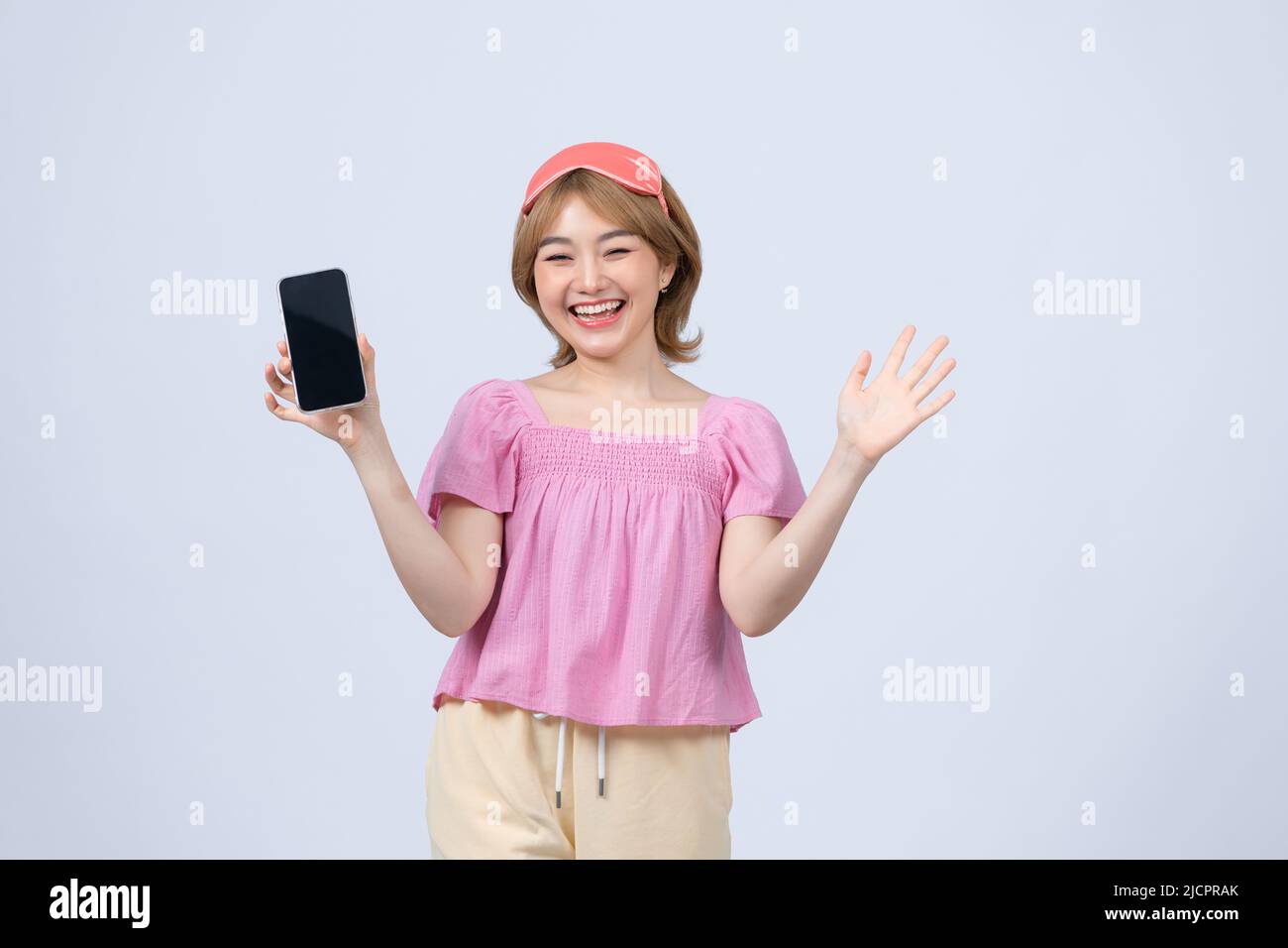 allegro sorridente donna tenere in mano smartphone mobile con schermo nero vuoto indossare maschera di sonno isolato su sfondo bianco Foto Stock