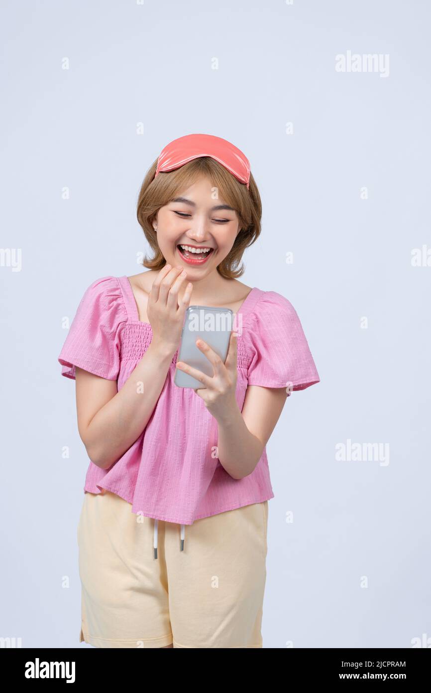 happy ragazza guardare la fotocamera tenere telefono cellulare in mani indossare rosa maschera di sonno ottenere buone notizie Foto Stock