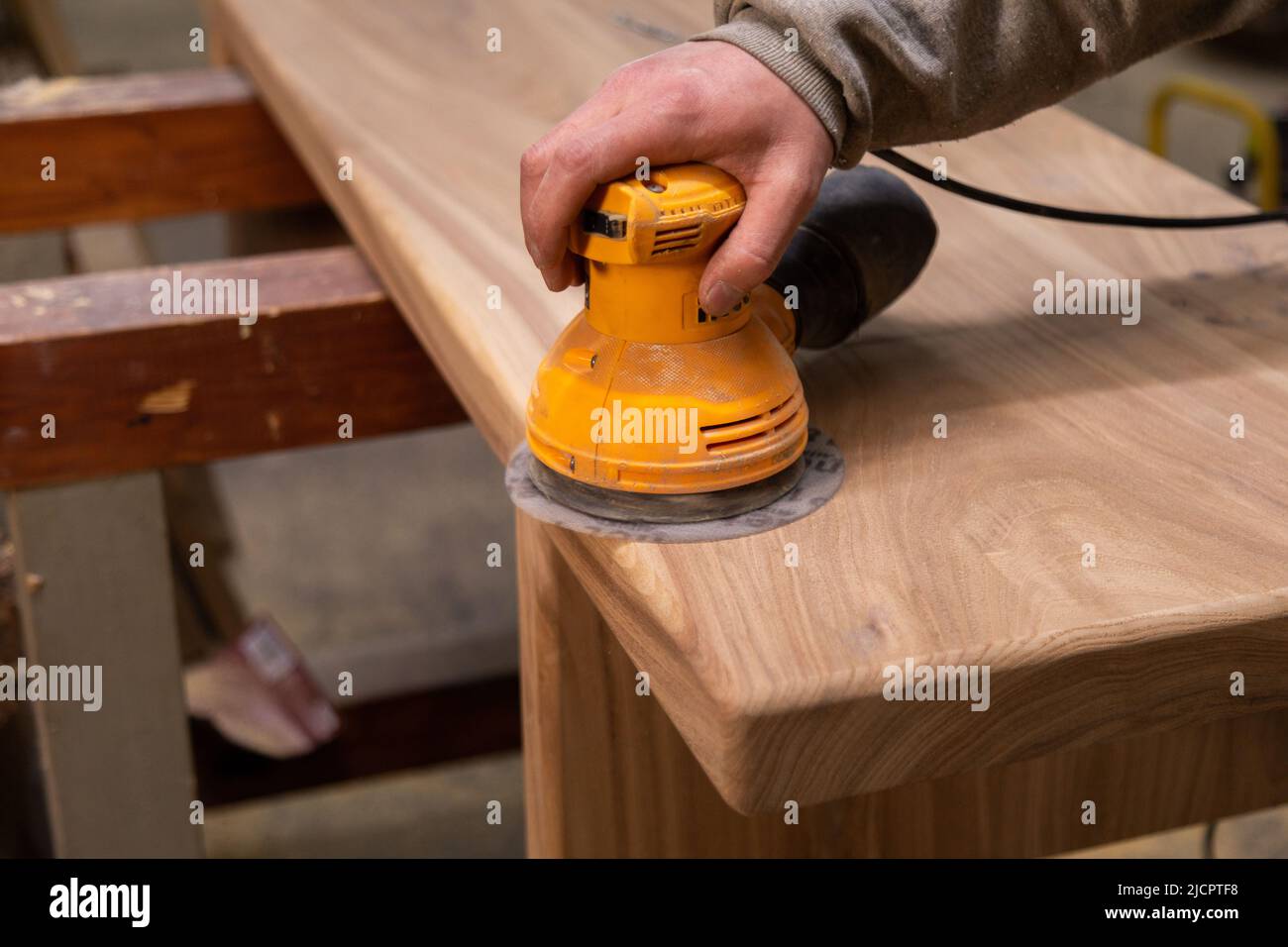 Primo piano di carteggiatura del tavolo in legno con levigatrice orbitale in un'officina Foto Stock