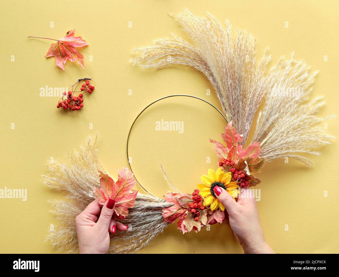 Mani che fanno la corona floreale asciugata da pampas erba asciutta e foglie d'autunno. Piatto su carta gialla, luce del sole con lunghe ombre. Foto Stock