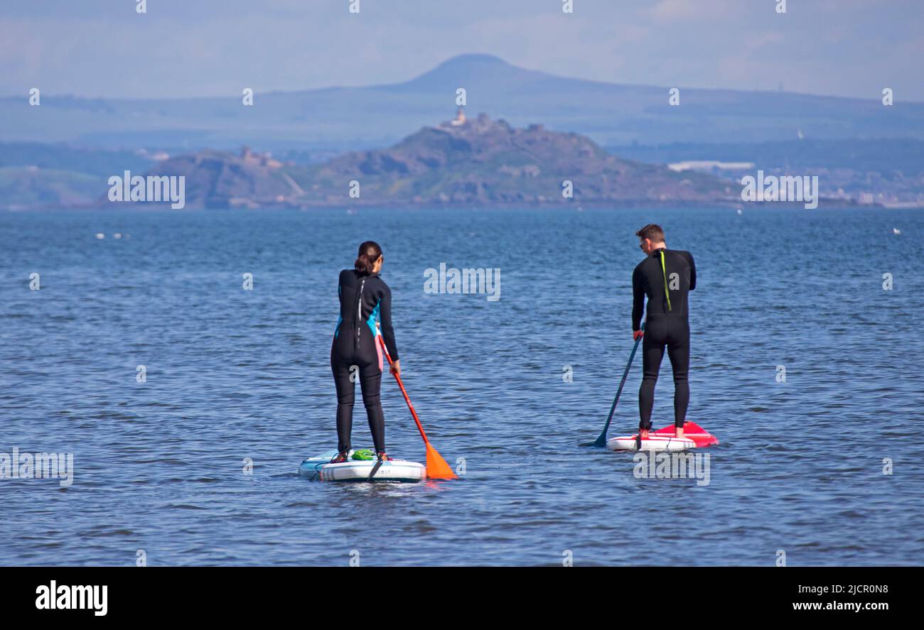 Portobello, Edimburgo, Scozia, Regno Unito. 15.06.2022. L'onda di calore che attrarre i pedalò fuori sopra al Firth di Forth, è stata alcune settimane da quando alcuno si è avventurato fuori a causa delle recenti condizioni nuvolose fredde. La temperatura di questa mattina di 18 gradi ha portato alcuni fuori per l'esercitazione. Nella foto: Paddleboarder maschili e femminili con l'isola Inchkeith sullo sfondo. Credit: Scottisgriative/alamy live news. Foto Stock