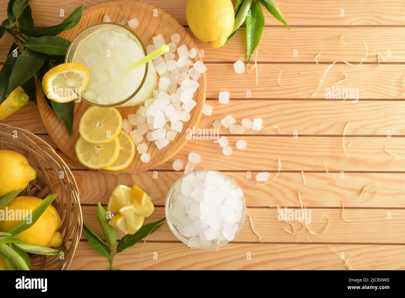 Sfondo con limonata con ghiaccio in un bicchiere su un tavolo di legno con frutta tagliata e ghiaccio tritato. Vista frontale. Composizione orizzontale. Foto Stock