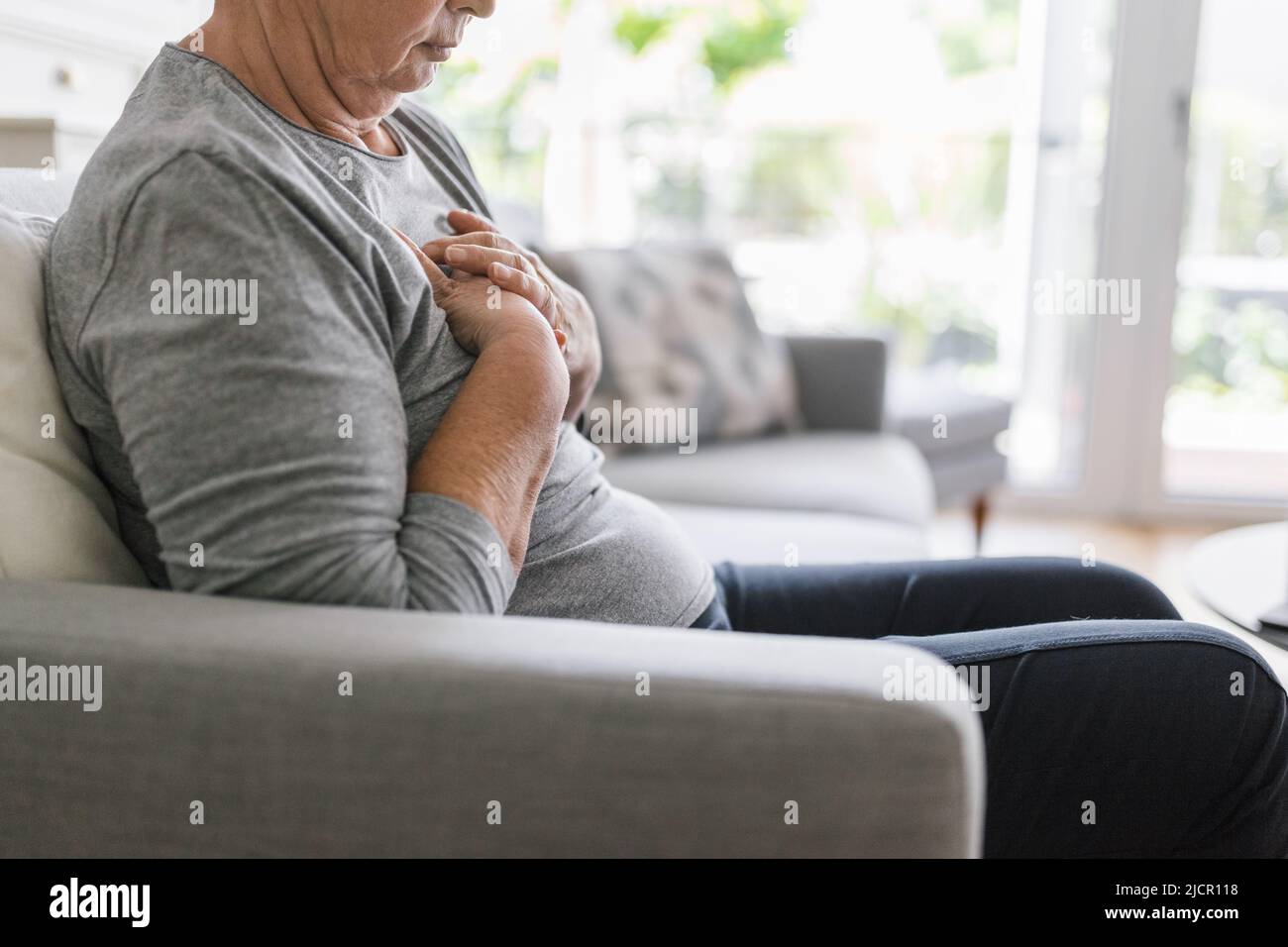 Donna anziana a casa con dolore al cuore che le tiene il petto Foto Stock