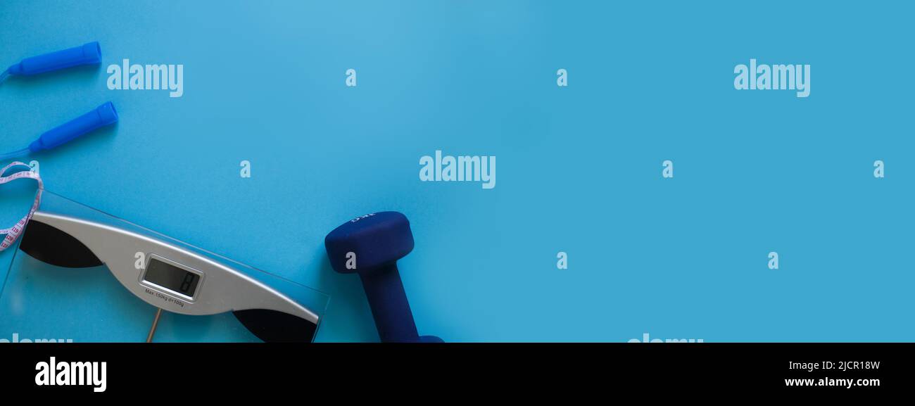 La donna misura il suo peso stando in piedi i piedi in calze su scala su uno sfondo blu con corda saltante e manubri. Composizione della disposizione piatta. Sano Foto Stock
