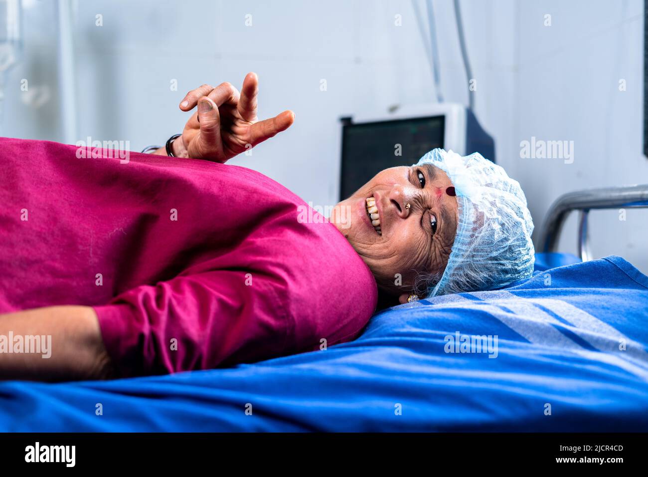 paziente malato anziano che mostra victroria o segno di v dopo un intervento chirurgico riuscito in ospedale mentre sul letto guardando il concetto di macchina fotografica di recupero, cura e. Foto Stock