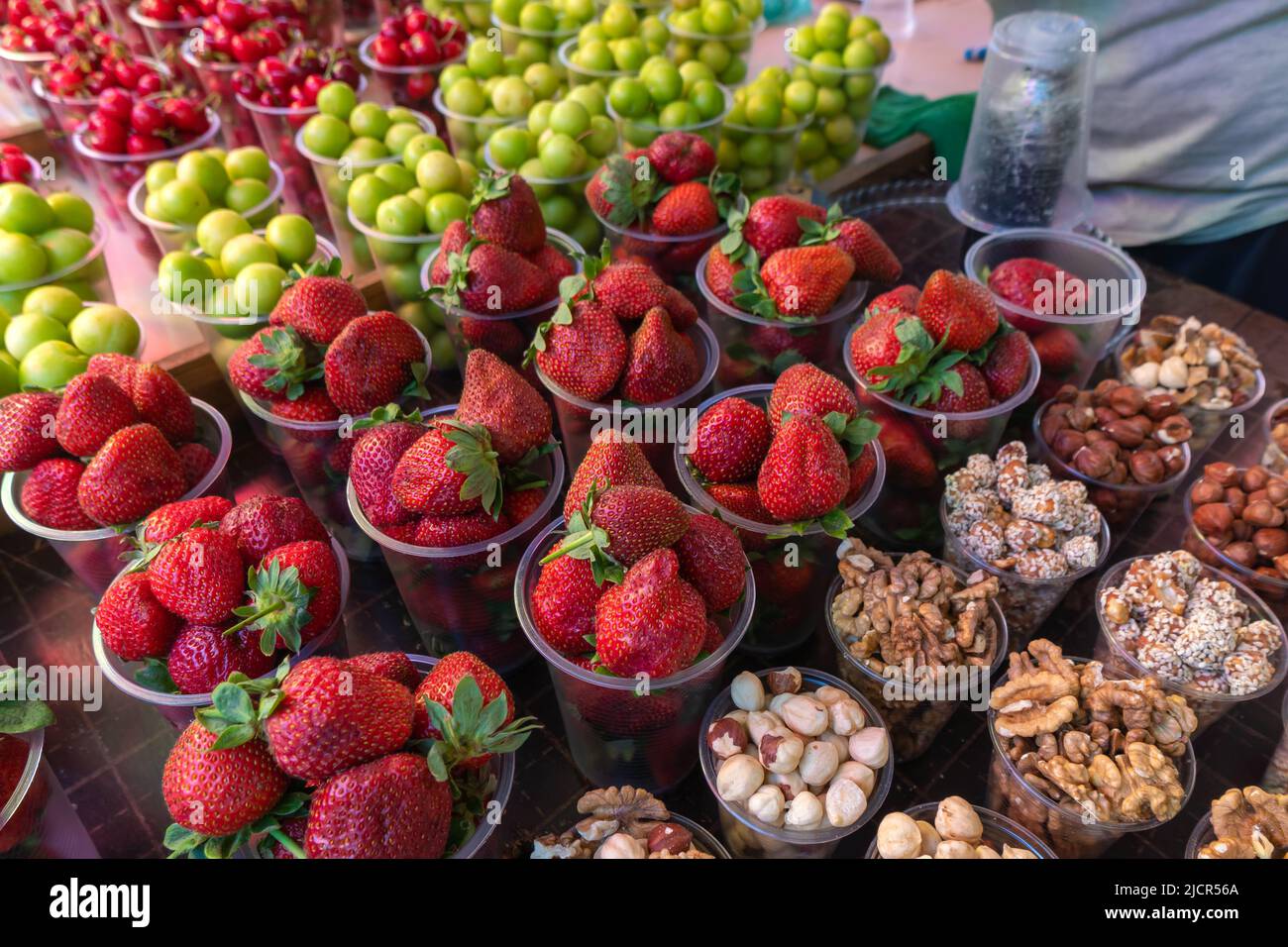 Primo piano di fragole, noci, frutta secca, ciliegie, nespola in coppe di plastica. Bancone con frutta, bacche e frutta secca, un luogo turistico. Foto Stock