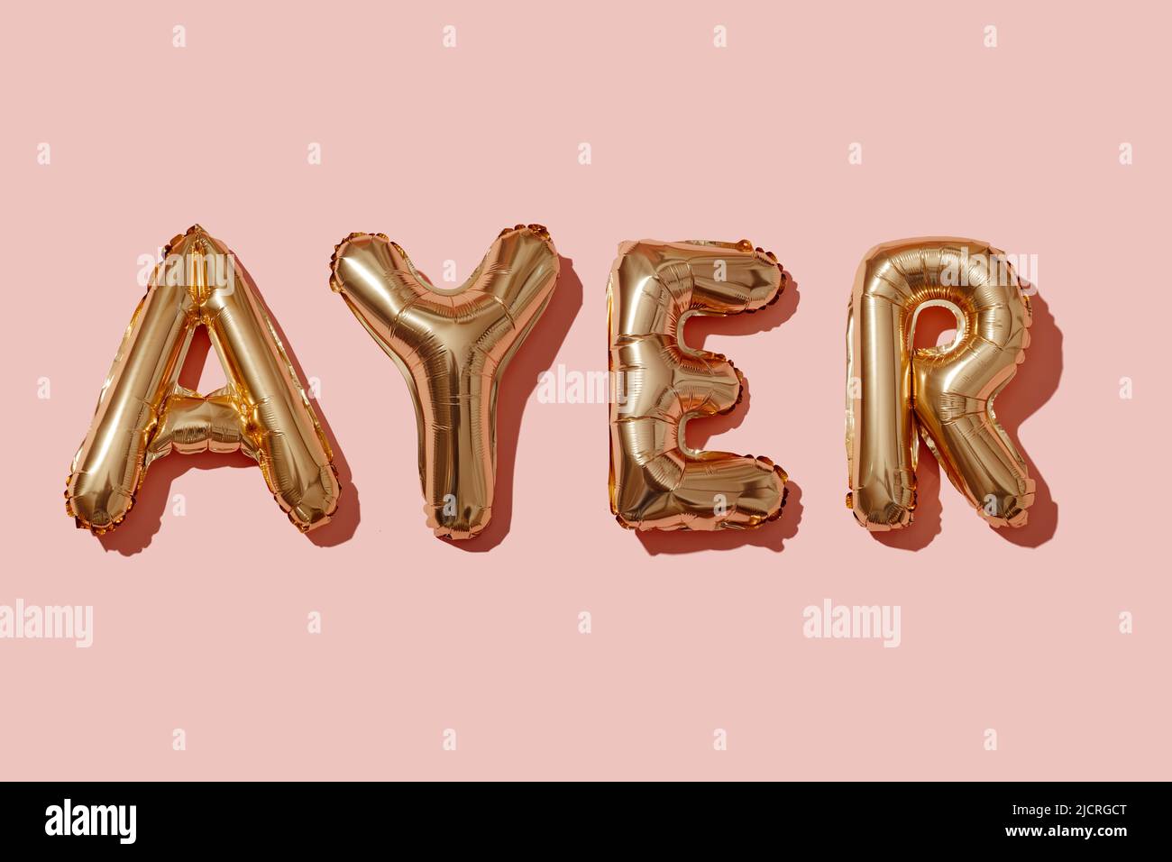 palloncini dorati a forma di lettera che formano la parola ieri in spagnolo su uno sfondo rosa Foto Stock