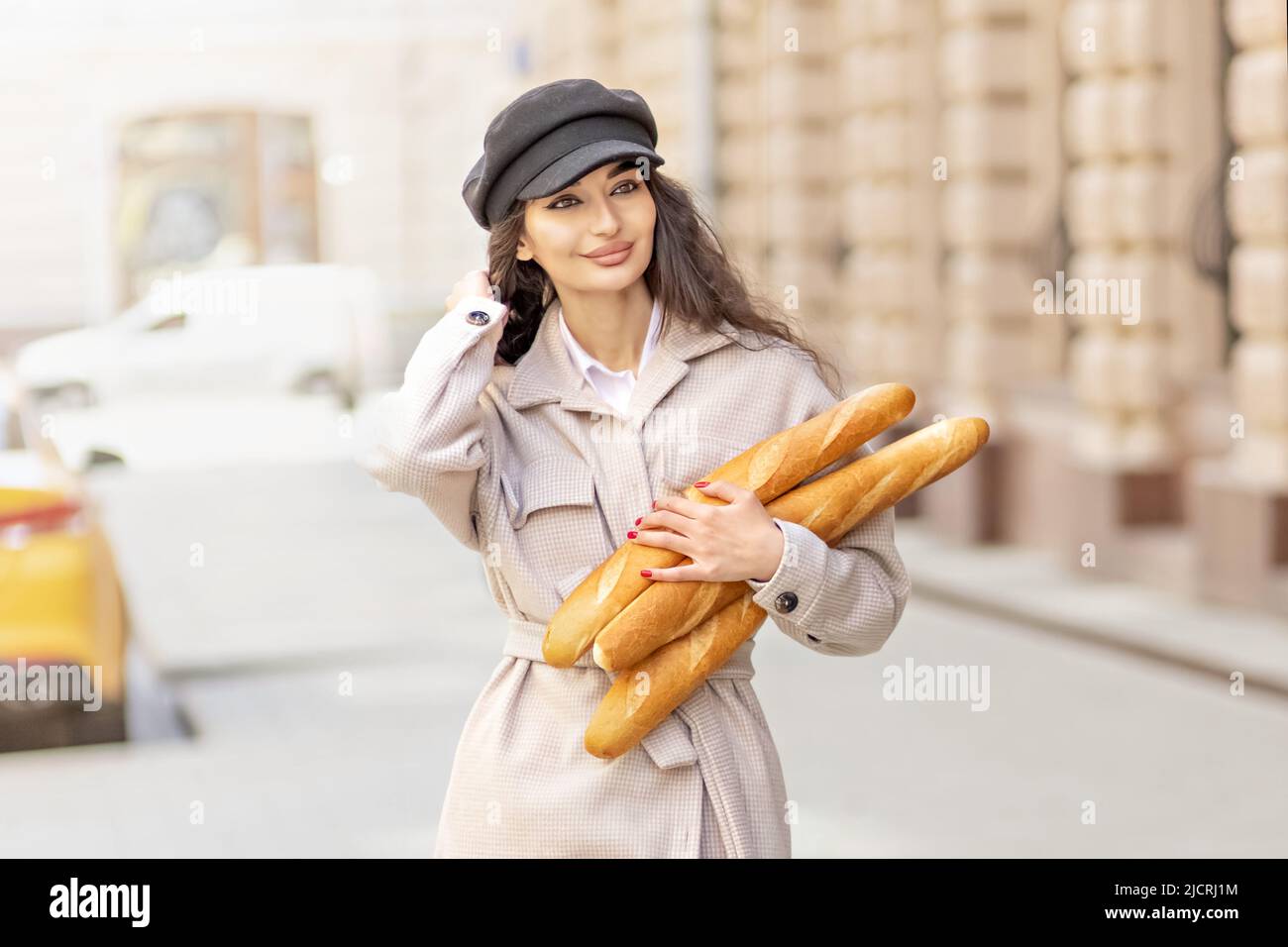 Ritratto di una giovane donna in un cappotto di primavera e cappuccio, con baguette in mano in città Foto Stock