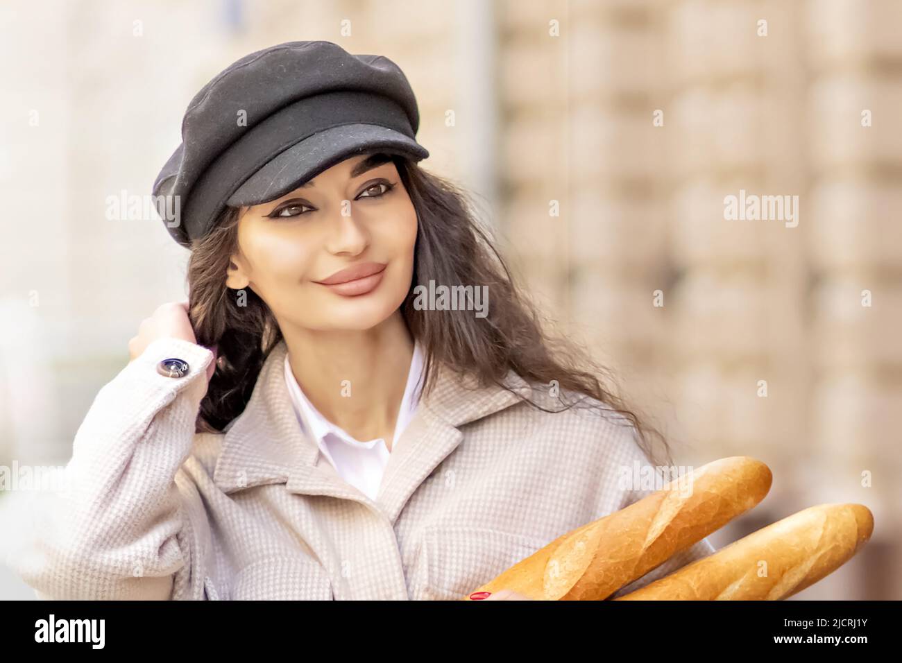 Ritratto di una giovane donna in un cappotto di primavera e cappuccio, con baguette in mano in città Foto Stock