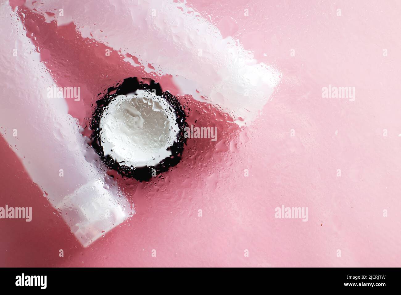 Concetto di prodotti naturali idratanti per la cura della pelle. Crema viso e mano sotto una superficie di vetro con acqua su sfondo rosa. Foto Stock