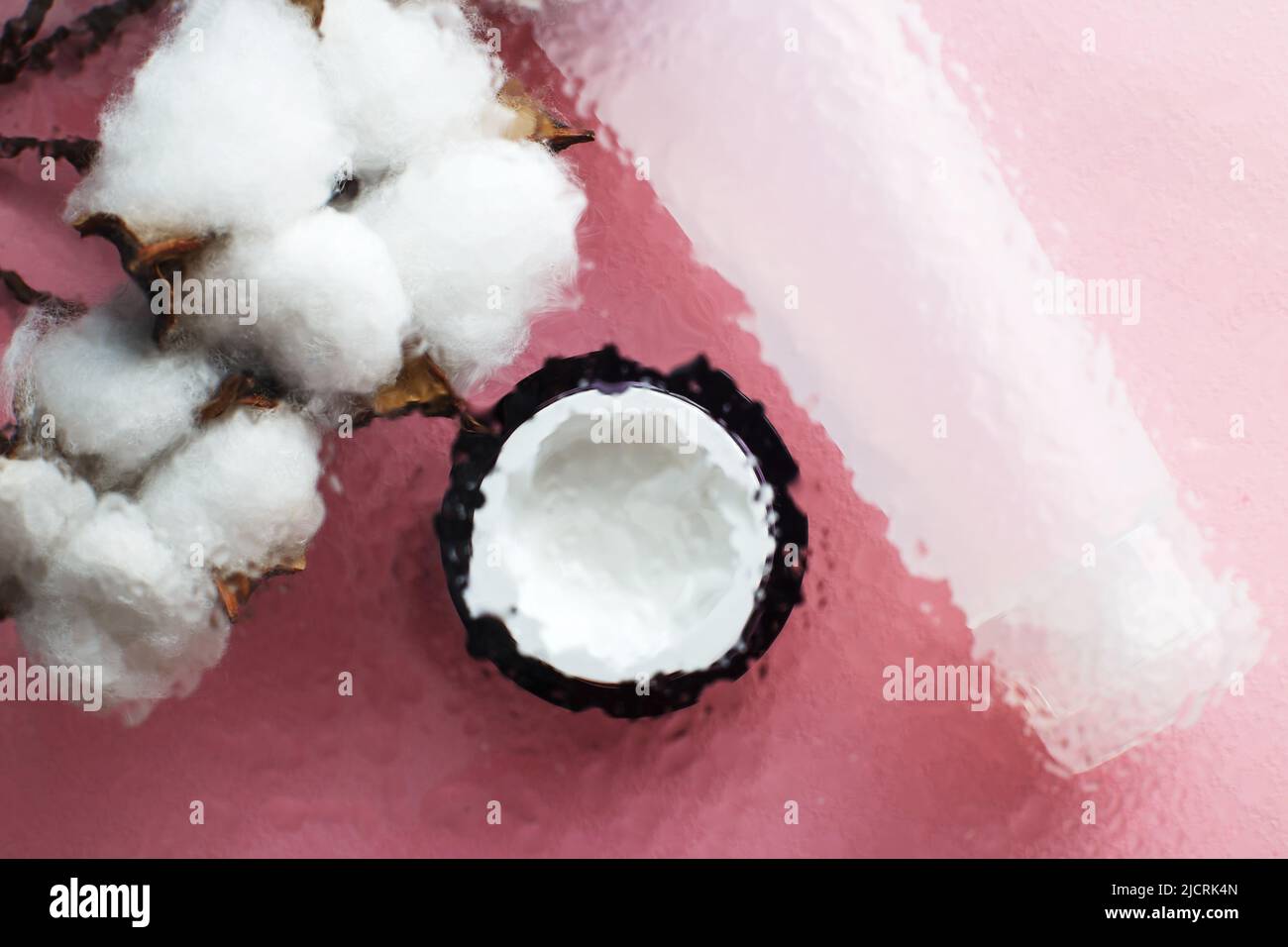 Concetto di prodotti naturali idratanti per la cura della pelle. Crema viso e mano sotto una superficie di vetro con acqua su sfondo rosa. Foto Stock