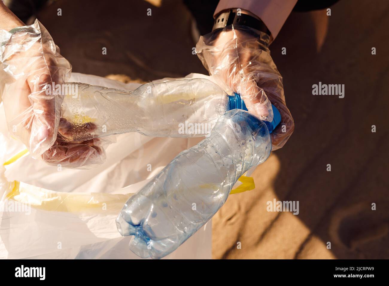 Mani umane tagliate in guanti di protezione che puliscono l'area sabbiosa da rifiuti di plastica. Raccogliere il flacone nel sacchetto. Problema ECO Foto Stock