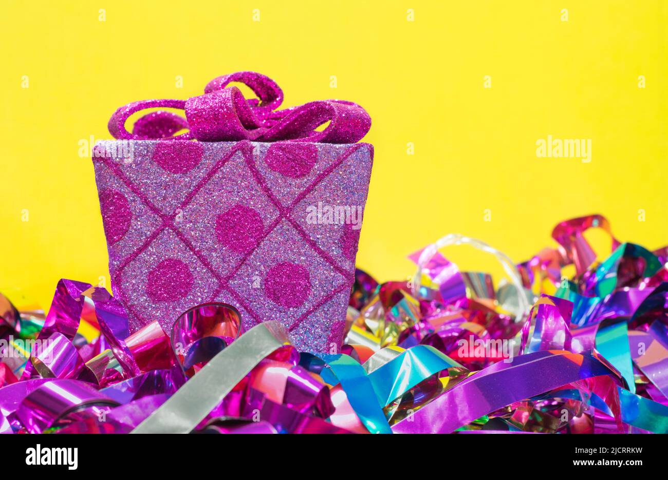 Avvolti regalo rosa decorativo e arco con nastri colorati sotto su uno sfondo giallo con spazio copia. Foto Stock