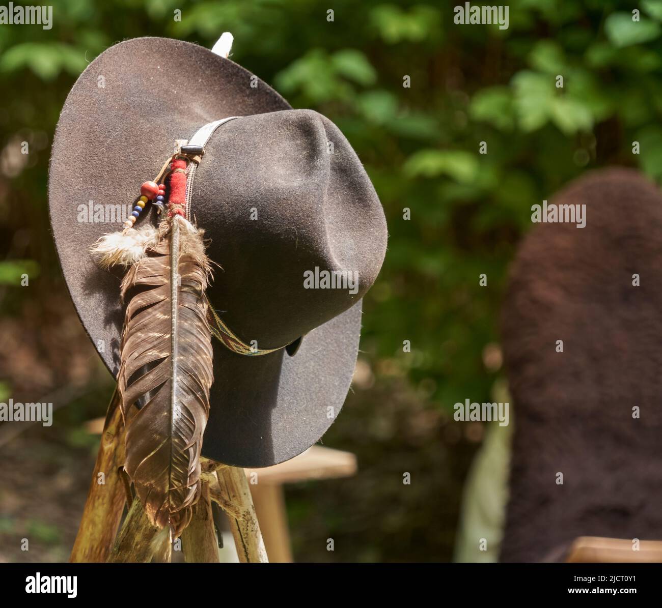 Cappello grigio con perline colorate e una lunga piuma di un uccello appende su un palo contro uno sfondo sfocato Foto Stock