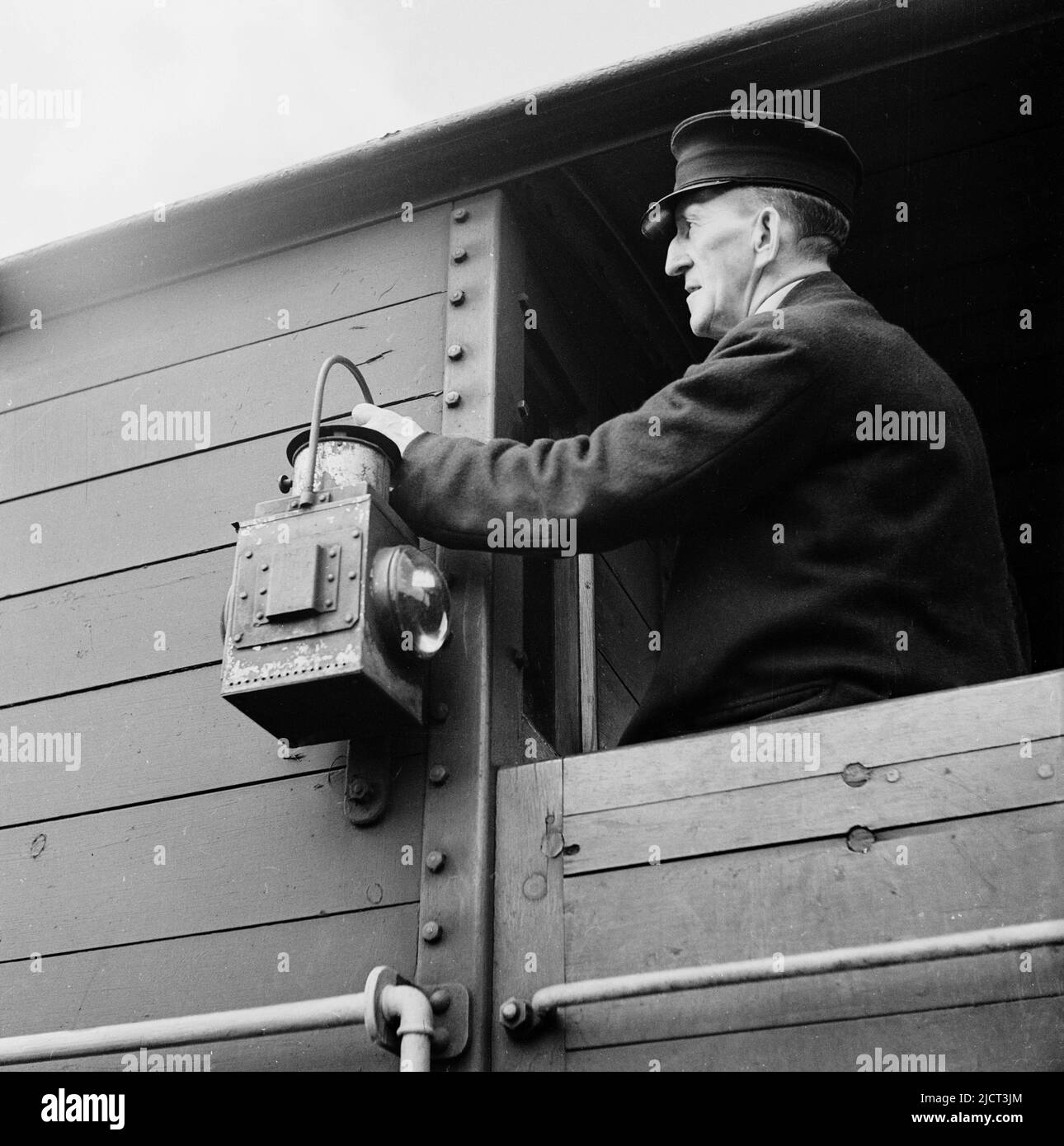 1950s, storica, una guardia ferroviaria in uniforme che fissa una lanterna di avvertimento sul lato di un trasporto merci delle ferrovie del grande ovest, banchine di Londra, Londra, Inghilterra, Regno Unito. Foto Stock
