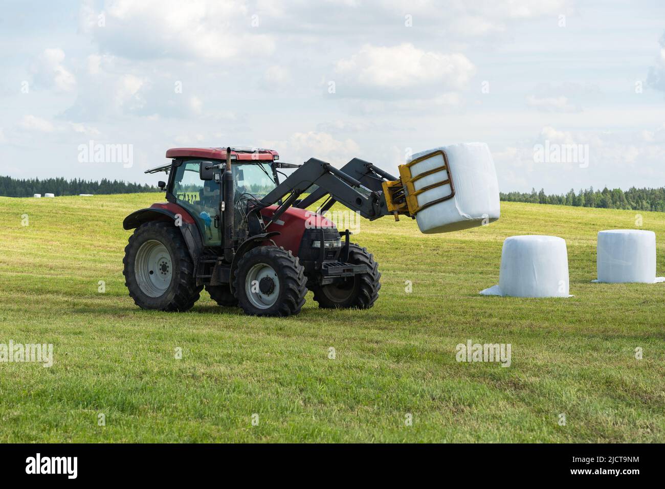 Agricoltore lituano che utilizza un trattore con movimentatore frontale per caricare le balle di fieno sul rimorchio. Foto Stock