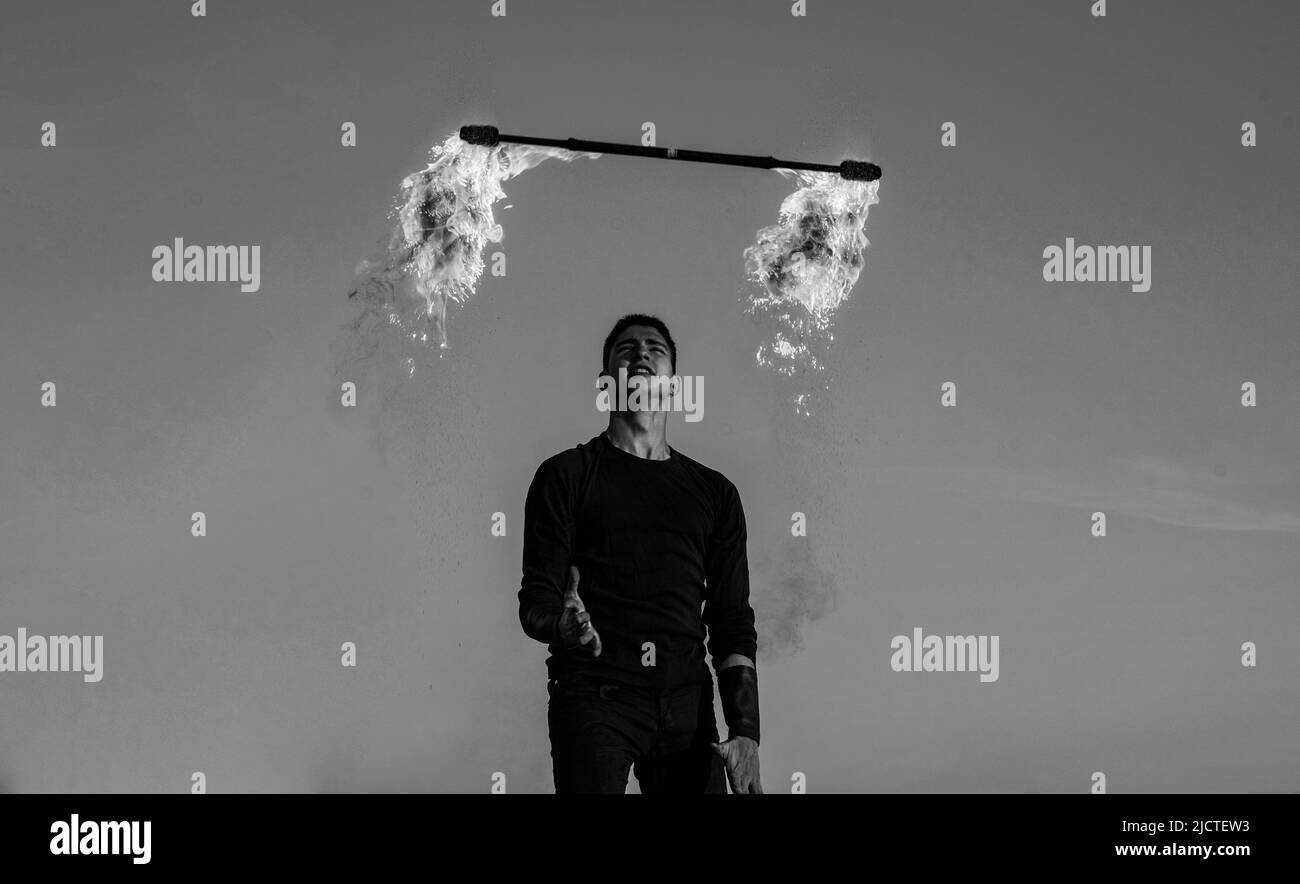 Uomo fuoco performer manipolare con fiammeggiante batone su cielo blu all'aperto, uomo Foto Stock