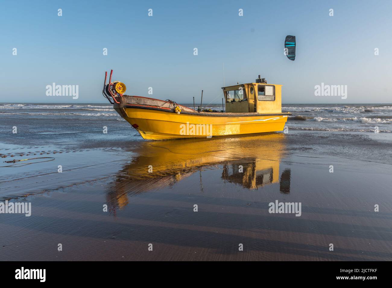 Barca da pesca sulla spiaggia con il mare e un kitesurfer sullo sfondo Foto Stock