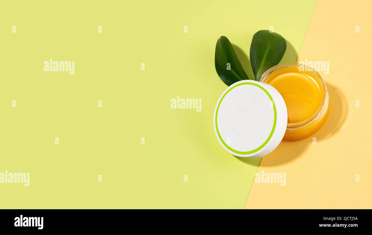 Un barattolo aperto di balsamo di piede con grasso di lana di pecora. Lanolina cosmetici per auto-cura, un vaso di cera impermeabilizzante su sfondo verde chiaro e beige. Foto Stock