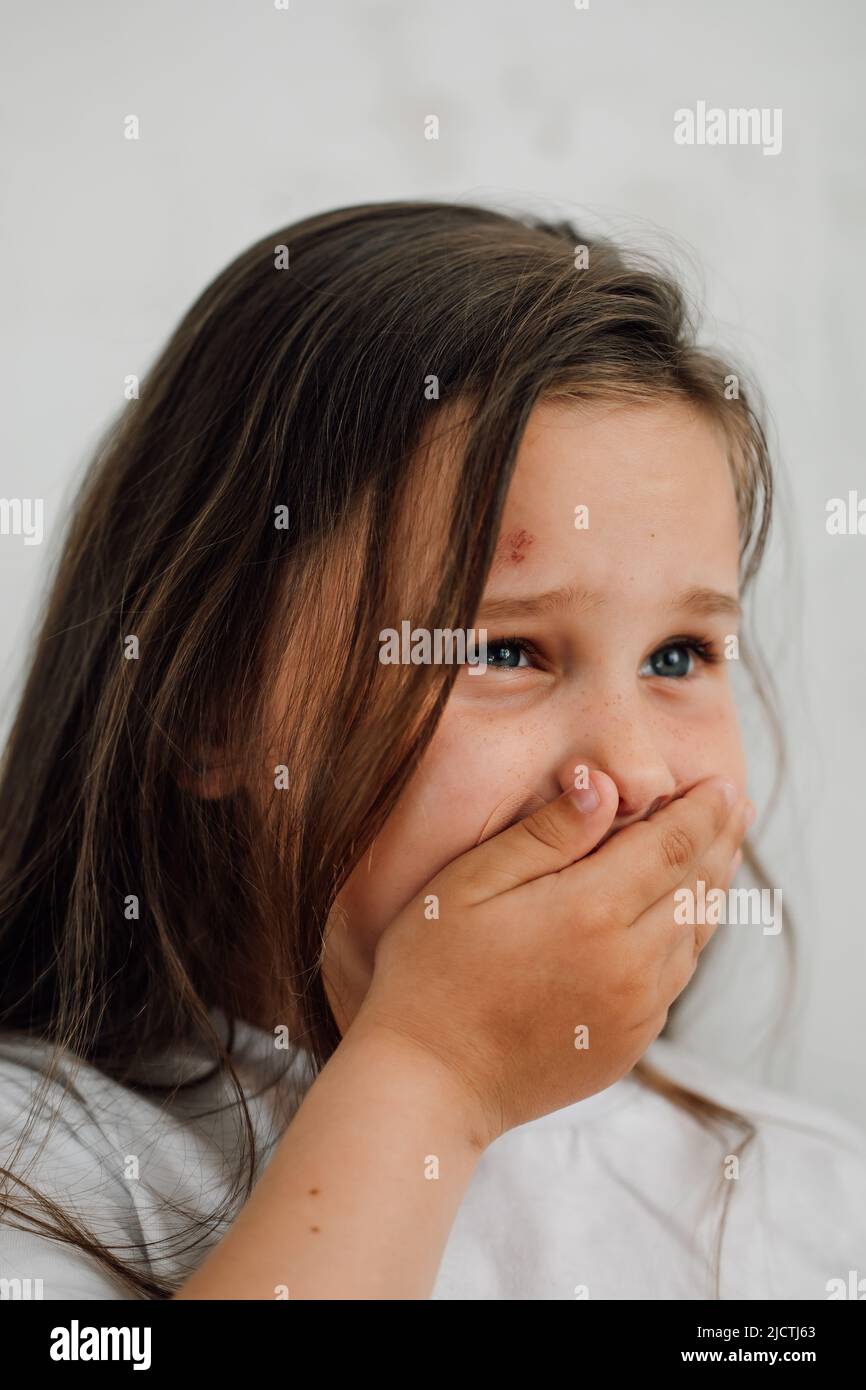 ritratto di piccola ragazza triste livida con capelli lunghi e scuri che ricoprono la bocca con la mano. Protesta contro gli abusi. Foto Stock