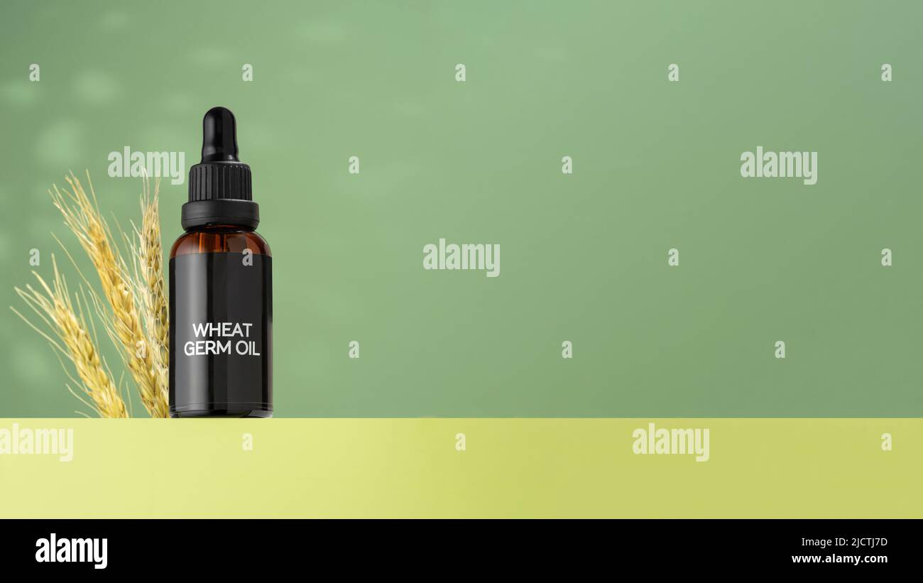 Bottiglia di vetro di olio di germogli di grano con contagocce, in piedi sul podio verde. Orecchie di germe di grano e una fiala di olio essenziale per uso cosmetico. Foto Stock
