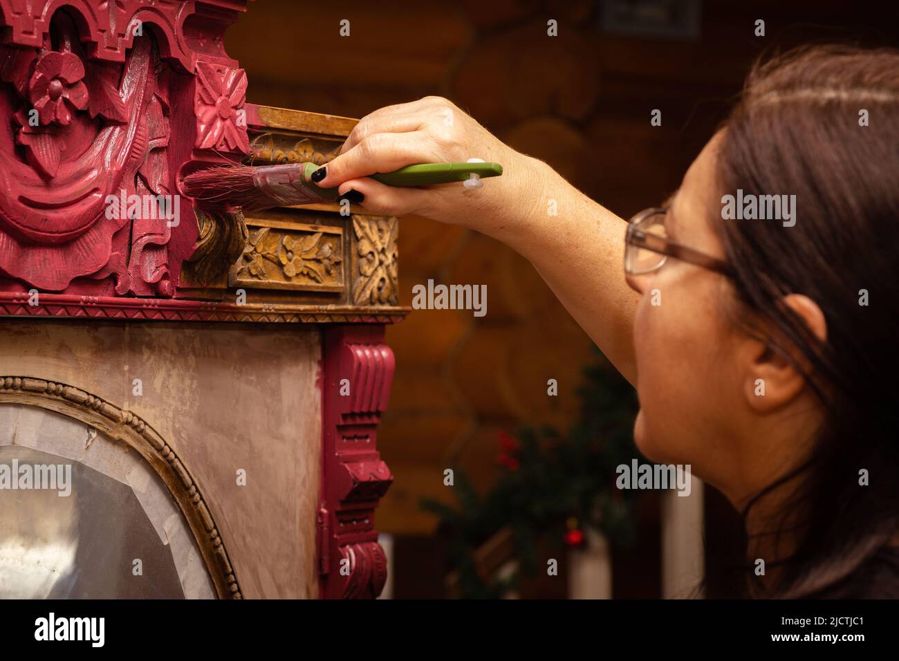 Donna in corso di verniciatura della parte superiore di legno ornato armadio in rosso con pennello in mano. Dare nuova vita alle cose antiche. Mobili per la casa Foto Stock