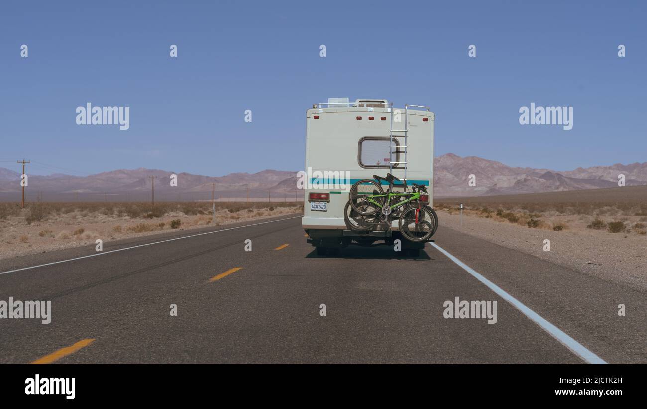 Nevada: Parte posteriore di un camper con due biciclette su un portabiciclette mostrato guidare su un'autostrada solitaria nel deserto in una giornata di sole. Foto Stock