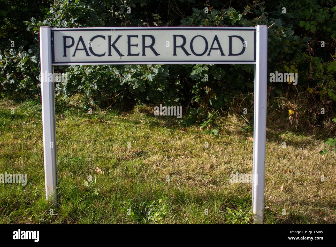 Cartello con il nome della strada del packer Road su due montanti con erba e una siepe sullo sfondo Foto Stock