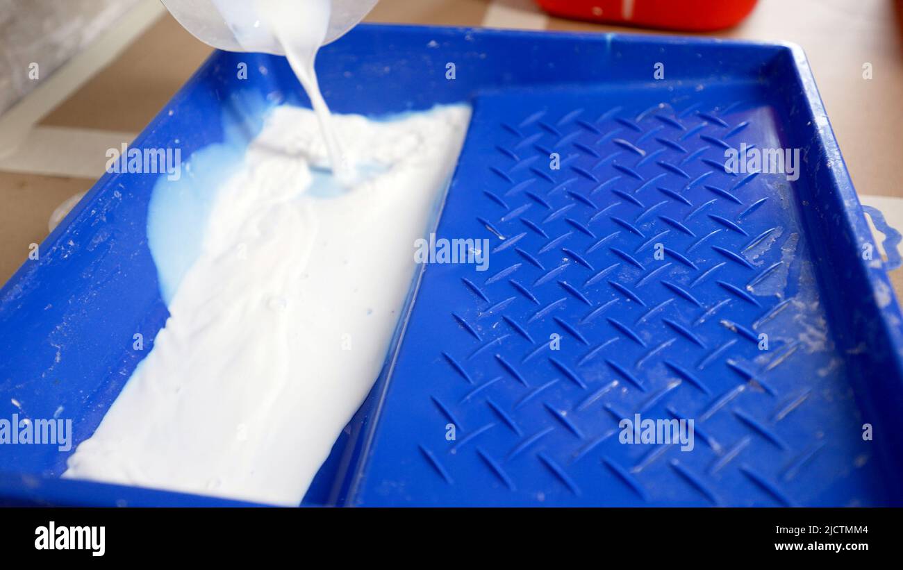 Una soluzione bianca viene versata nei bagni per cementare la cucitura tra le piastrelle. Il cartongesso versa il primer dal canister. Il lavoratore versa il prim Foto Stock