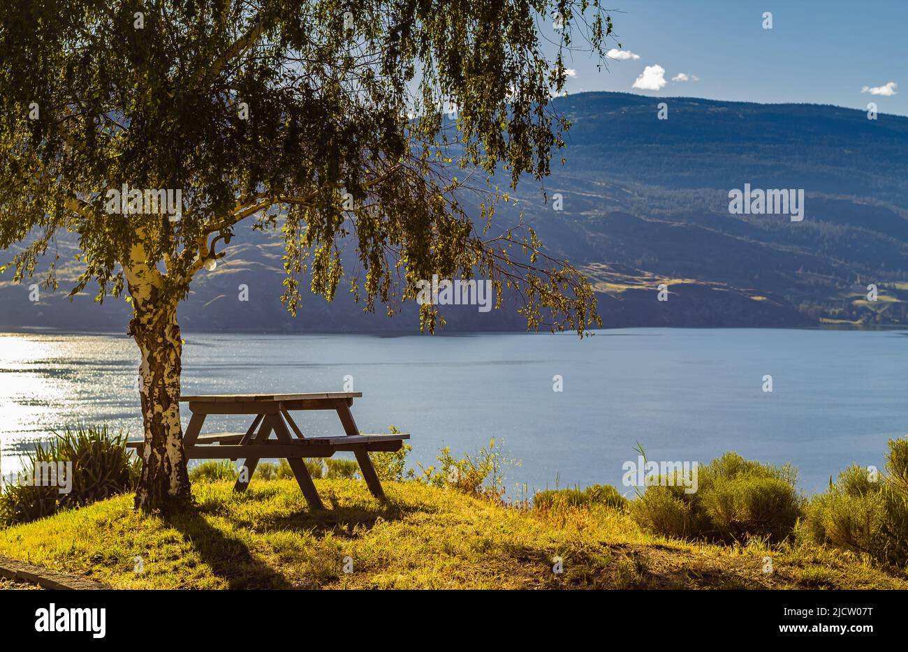 Tavolo vuoto in legno con sedie sulla collina di un parco estivo al lago Okanagan BC Canada. Giornata calda di sole vicino al lago. Paesaggio alba mattina. Tra Foto Stock