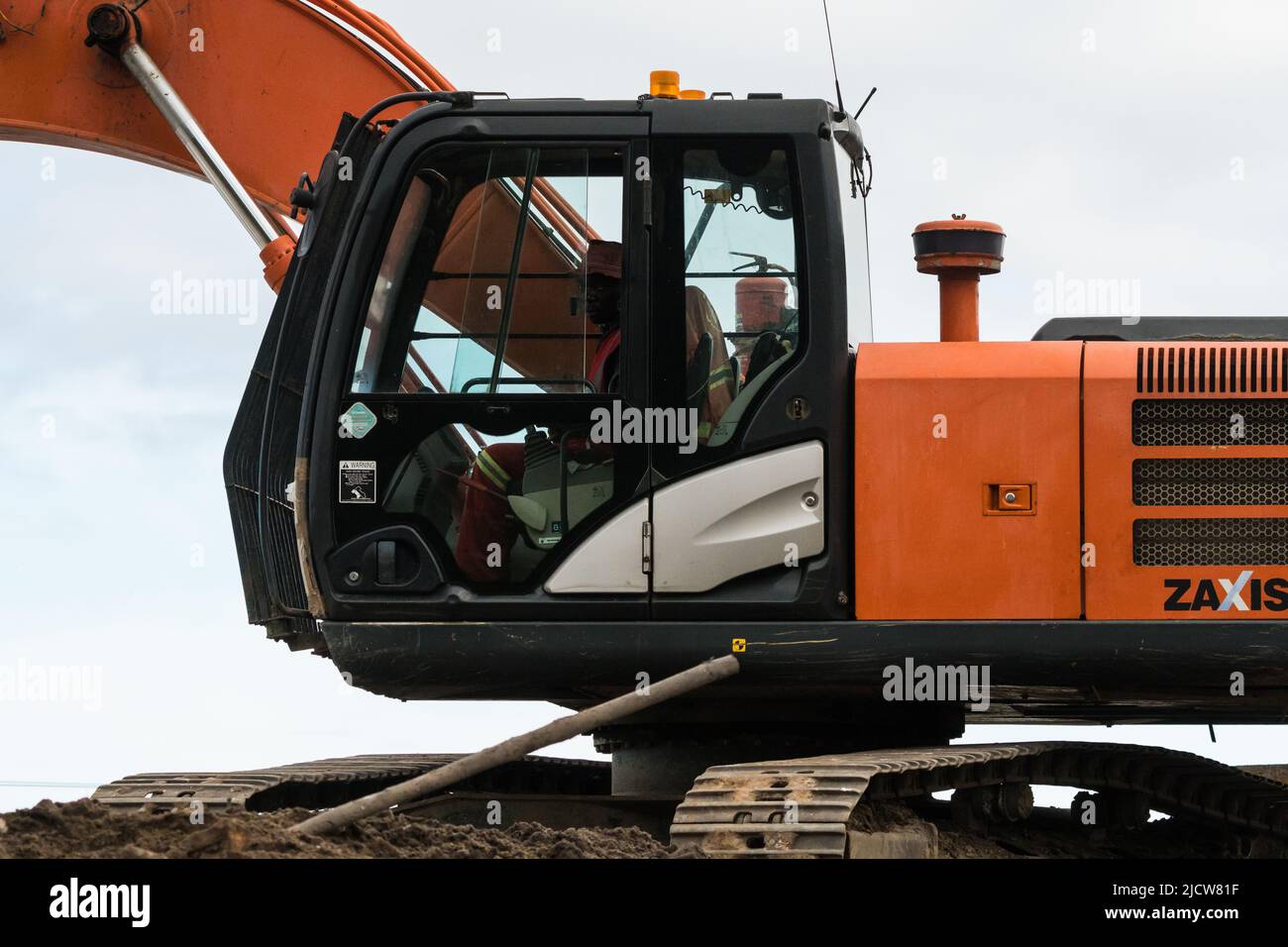 Uomo africano, dipendente, lavoratore che opera macchinari meccanici pesanti o bulldozer closeup nel settore delle costruzioni in Sud Africa Foto Stock