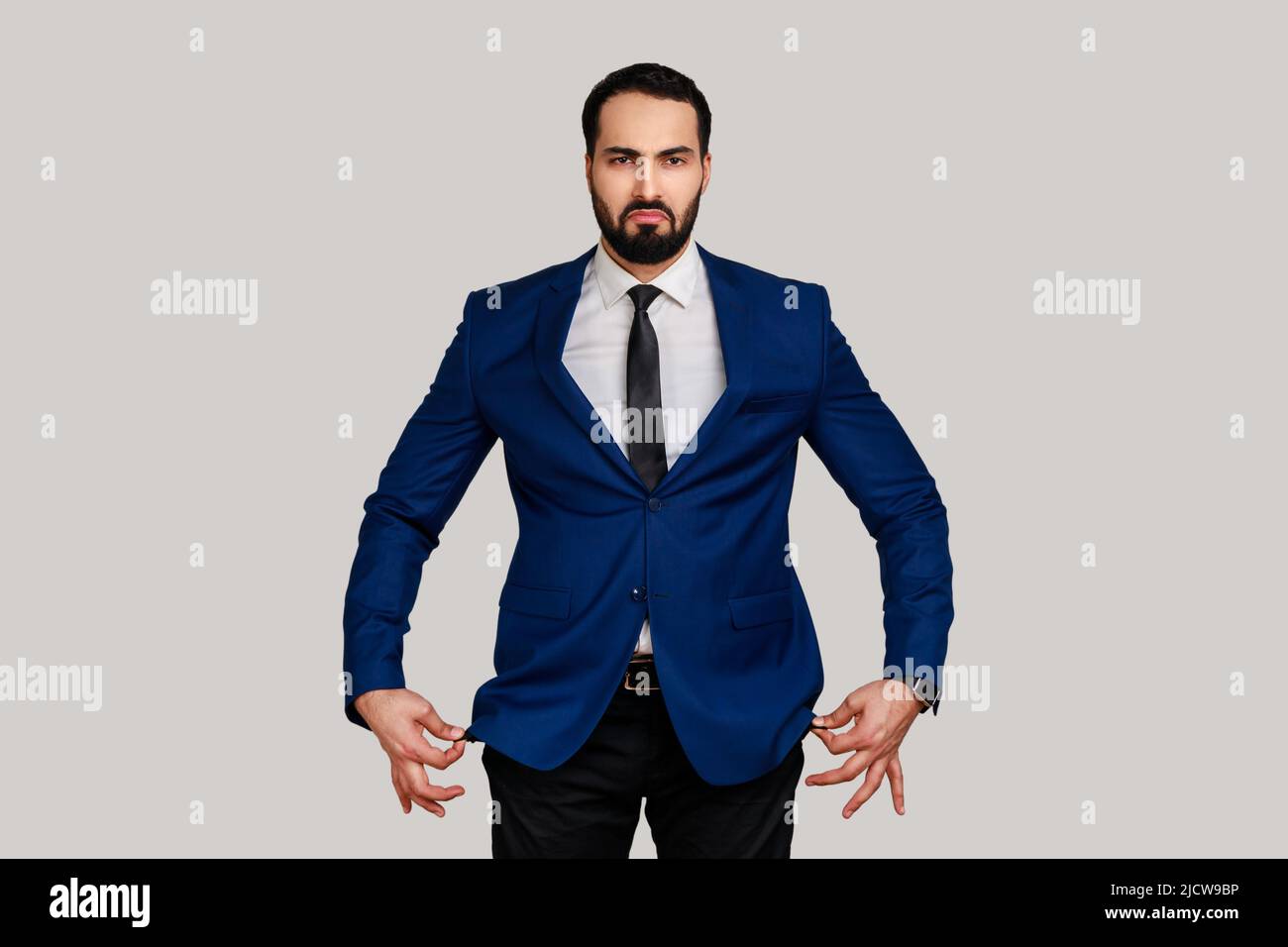 Ritratto di triste infelice uomo barbuto mostrando tasche vuote all'interno, andando in bancarotta, senza contanti per vivere, indossando vestito di stile ufficiale. Studio interno girato isolato su sfondo grigio. Foto Stock