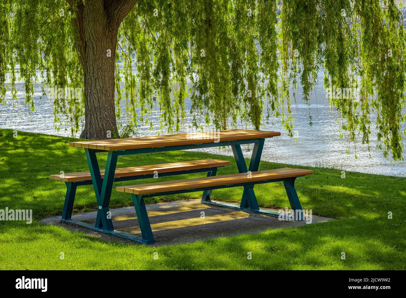 Tavolo vuoto in legno con sedie in un parco estivo al lago Okanagan BC Canada. Giornata calda di sole vicino al lago. Paesaggio alba mattina. Foto di viaggio, n Foto Stock