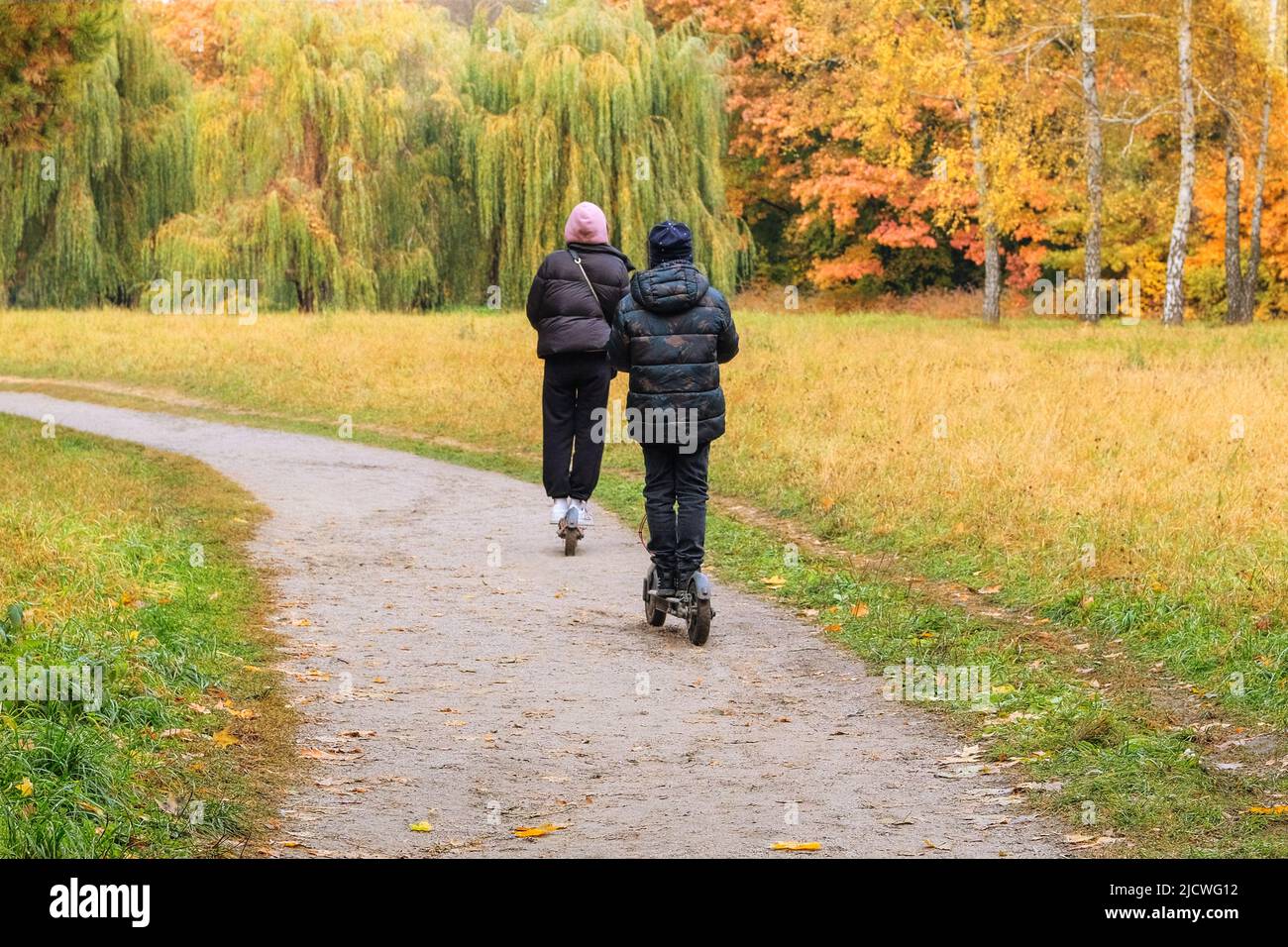 I bambini cavalcano uno scooter elettronico nel parco in autunno. Parco autunnale della città. Settembre, ottobre, novembre. Foto Stock