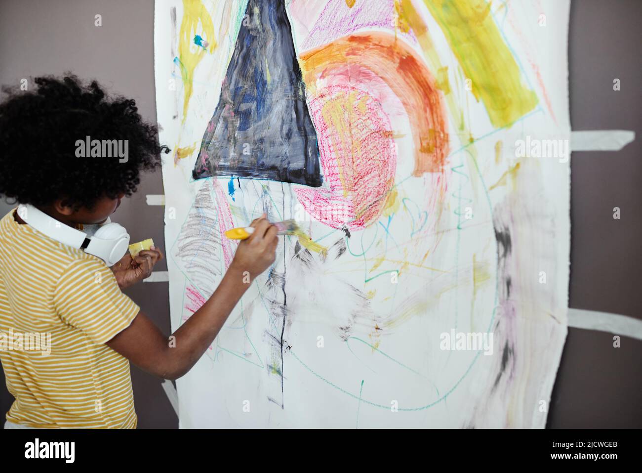 Ragazzino africano che usa il pastello giallo per disegnare un'immagine su carta grande appesa al muro Foto Stock