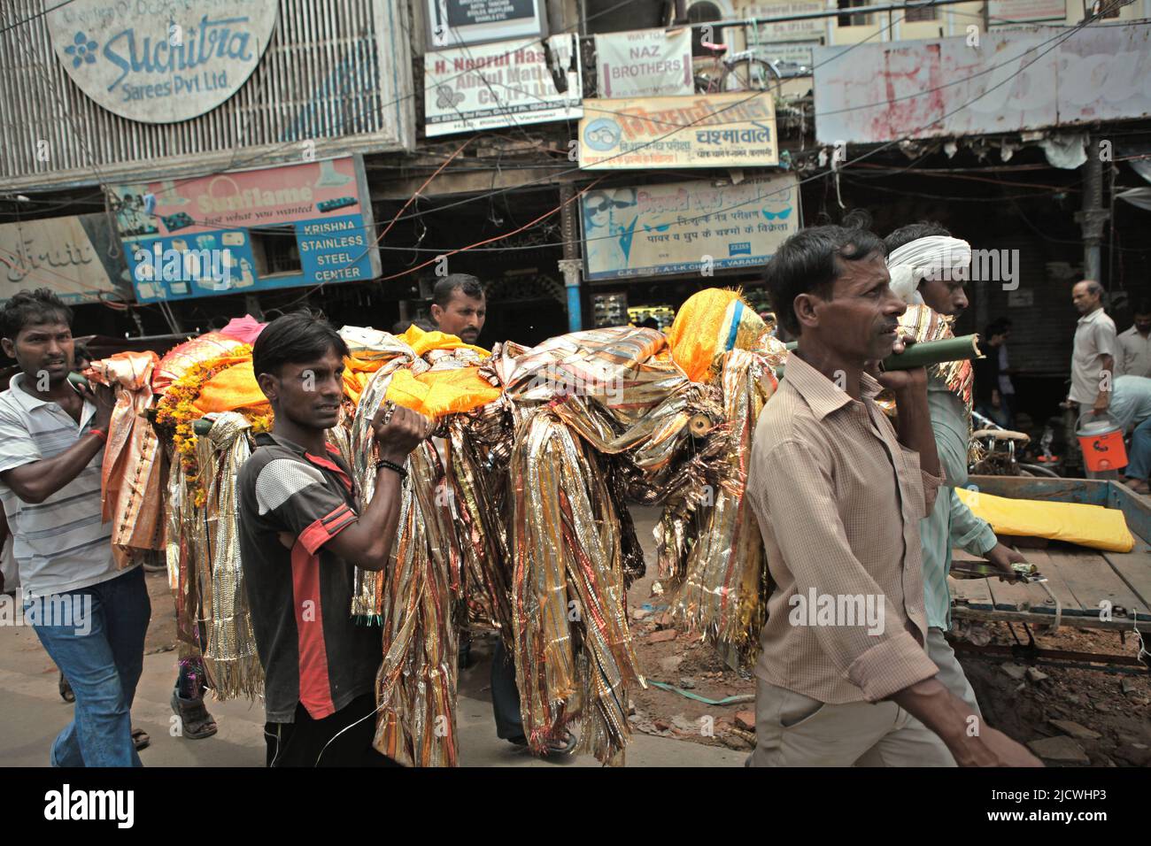 Gli uomini che trasportano un corpo mentre stanno camminando su una strada trafficata, dirigendosi verso uno dei ghat di cremazione sulla riva del fiume Ganges per la cremazione funeraria in Varanasi, Utar Pradesh, India. Foto Stock
