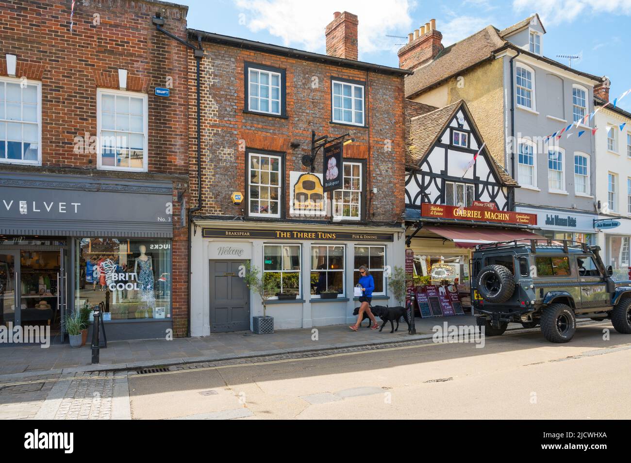 Il pub Three Tuns. Una donna con due cani neri Labrador su porta passa oltre. Market Place, Henley on Thames, Oxfordshire, Inghilterra, Regno Unito. Foto Stock