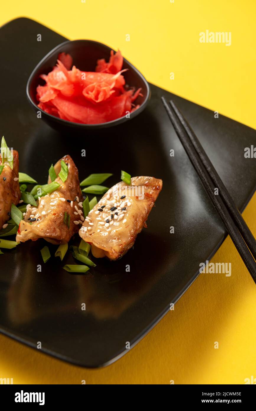 Gnocchi fritti asiatici Gyoza o Jiaozi con salsa di soia e cipolle verdi su sfondo di cemento nero, vista dall'alto Foto Stock