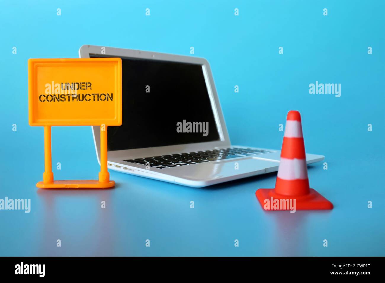 Sito web in costruzione concetto. Computer portatile, cono di sicurezza e cartello con testo IN COSTRUZIONE. Foto Stock