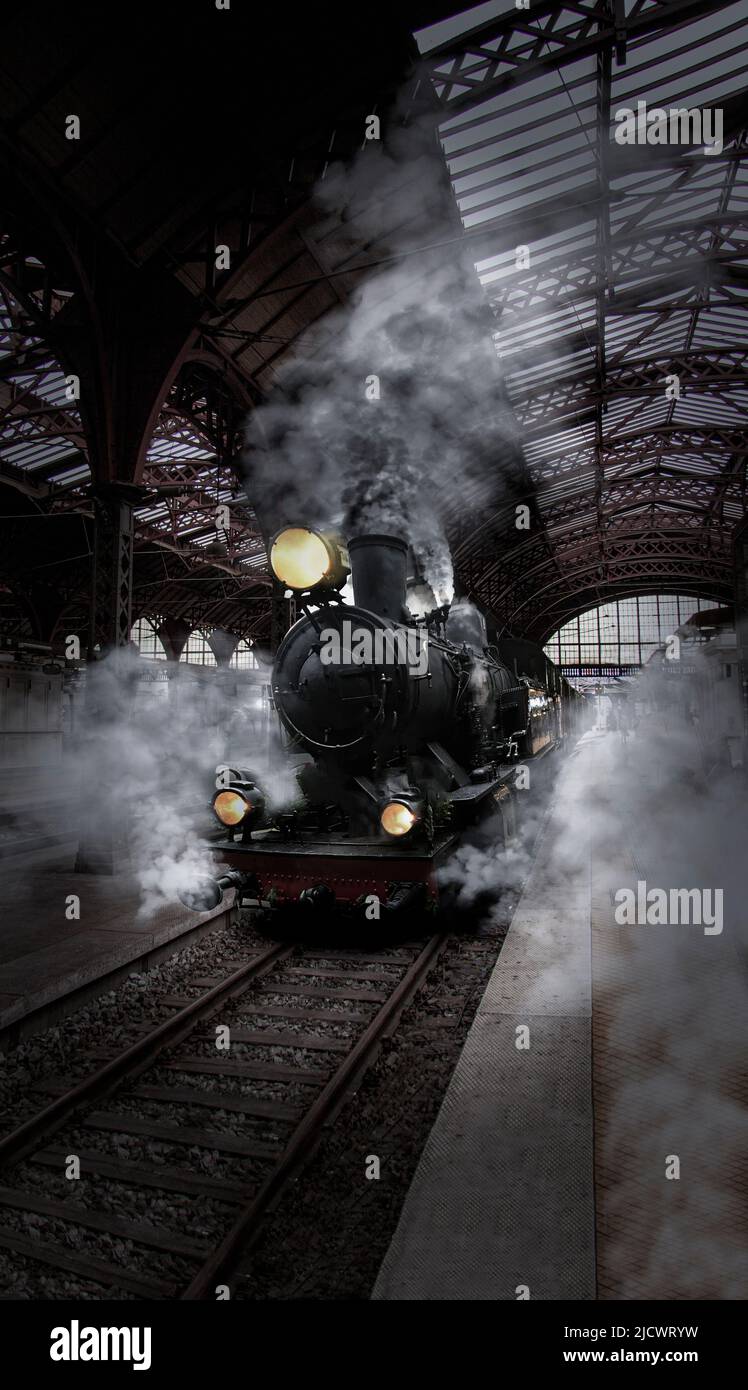Vista frontale di una locomotiva a vapore, treno veterano con molto stretto in una vecchia stazione ferroviaria in legno. Foto Stock