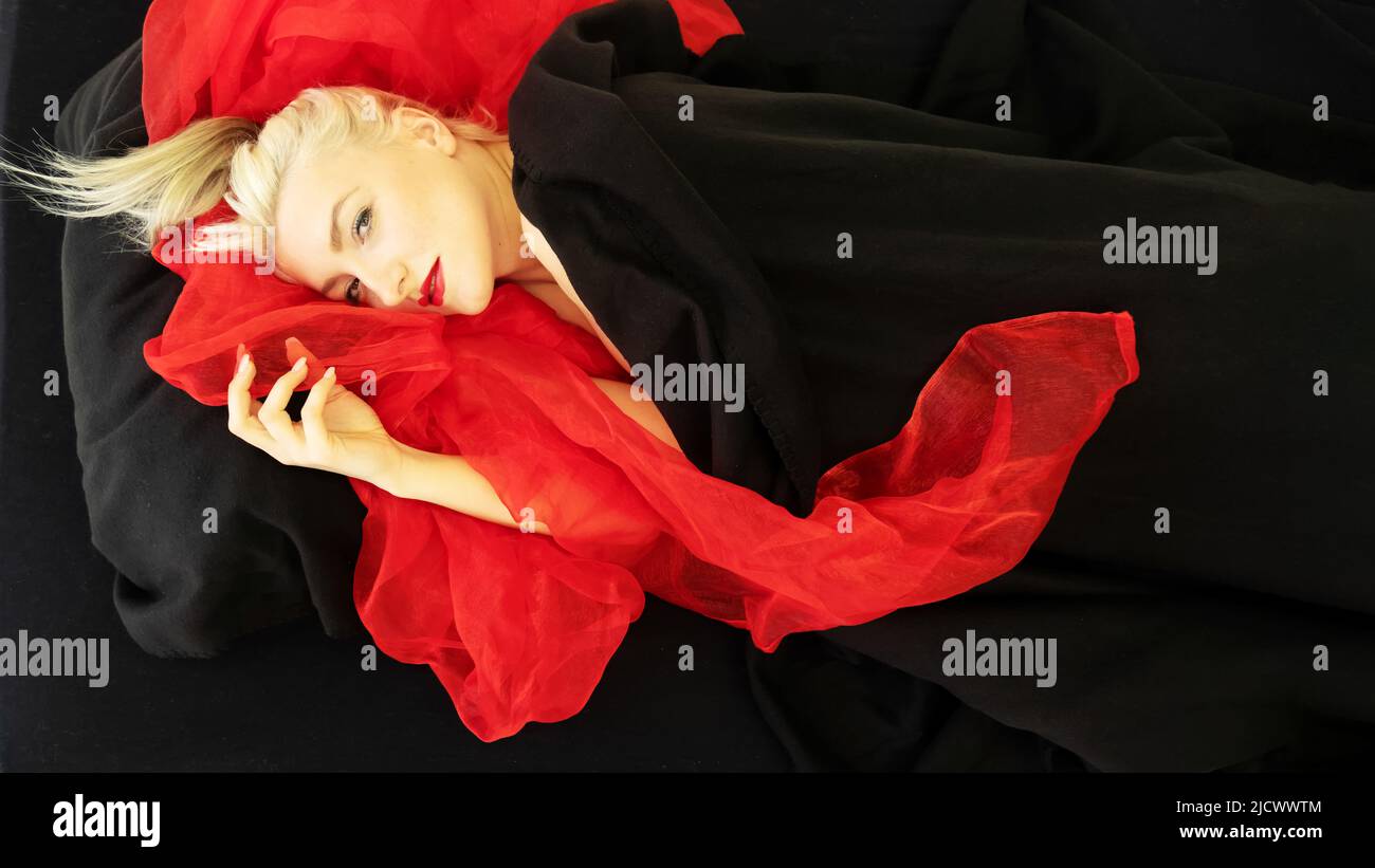sensuale, seducente ritratto di moda sexy di una giovane donna reclinata sexy, modello, sdraiato a letto, avvolto in stoffa nera e rossa, tessuto, spazio copia Foto Stock