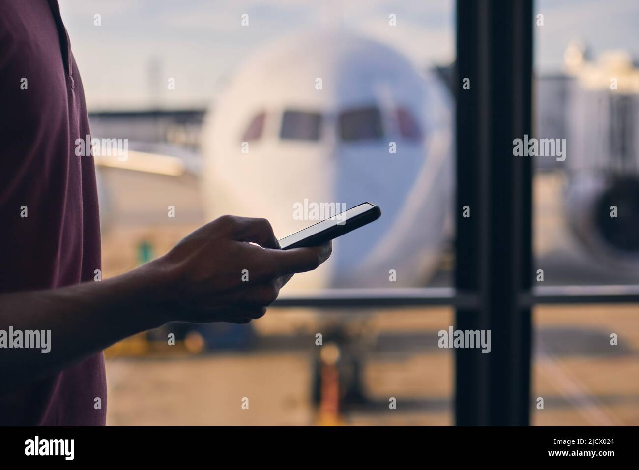 Silhouette della mano del passeggero mentre si utilizza il telefono cellulare durante l'attesa nel terminal dell'aeroporto. Foto Stock