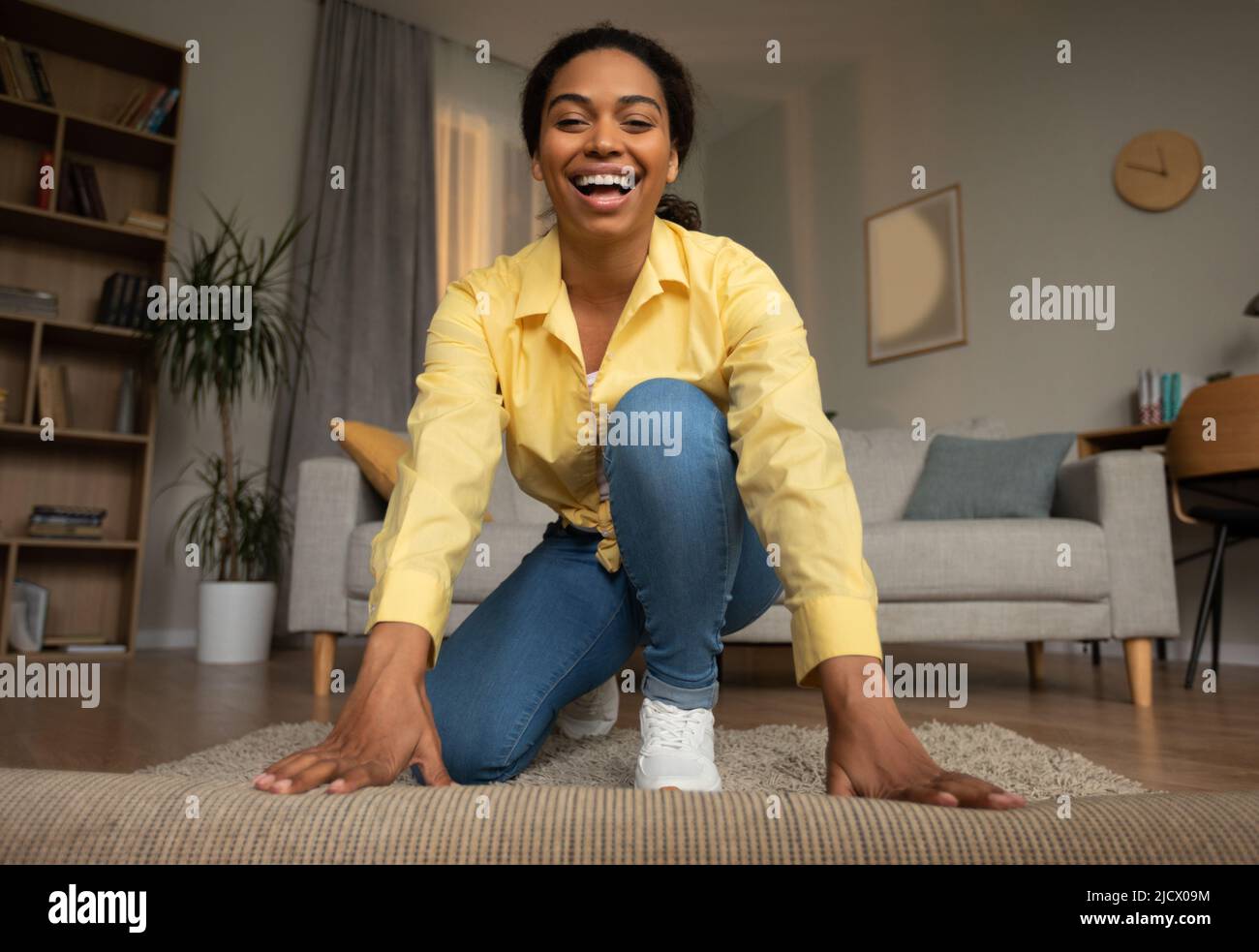 Joyful Black Lady Rolling out Carpet copertura pavimento a casa Foto Stock