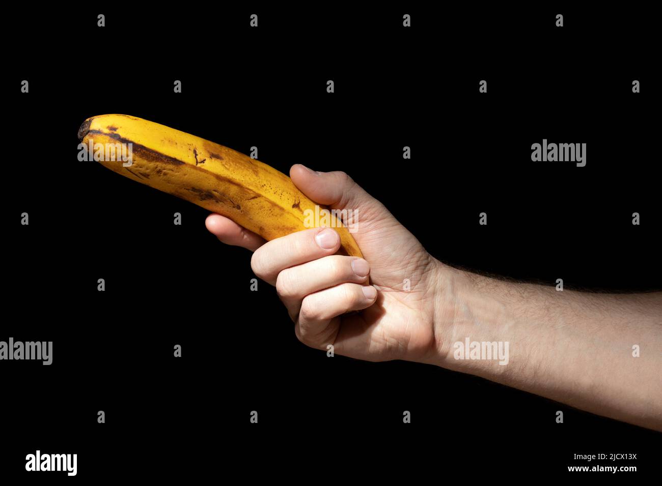 L'uomo tiene la banana matura in mano come una pistola su sfondo nero Foto Stock