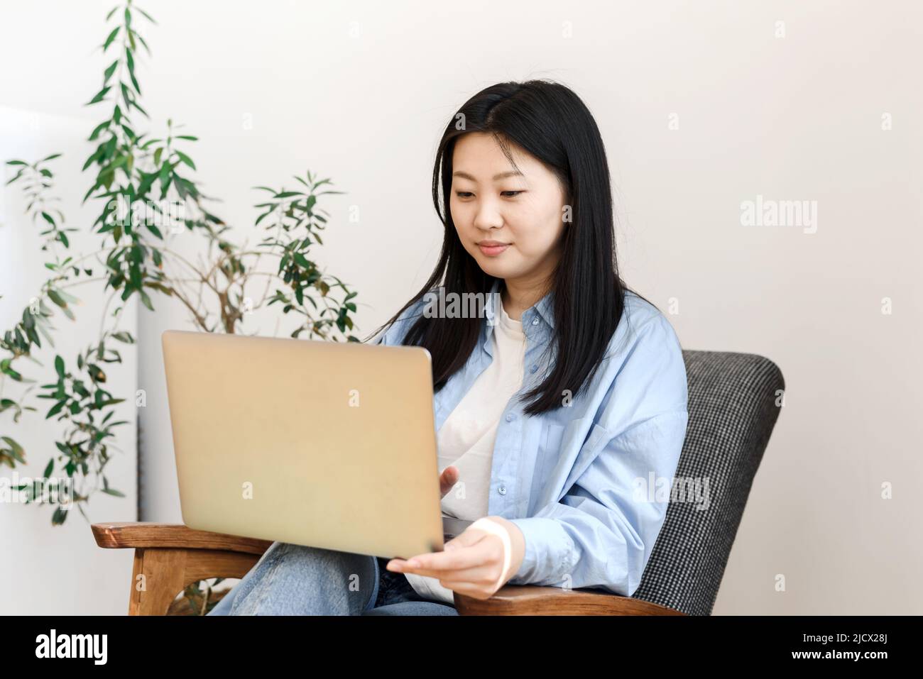 Concetto di freelance. La giovane donna asiatica si siede in una poltrona con un computer portatile che lavora a casa. Foto Stock