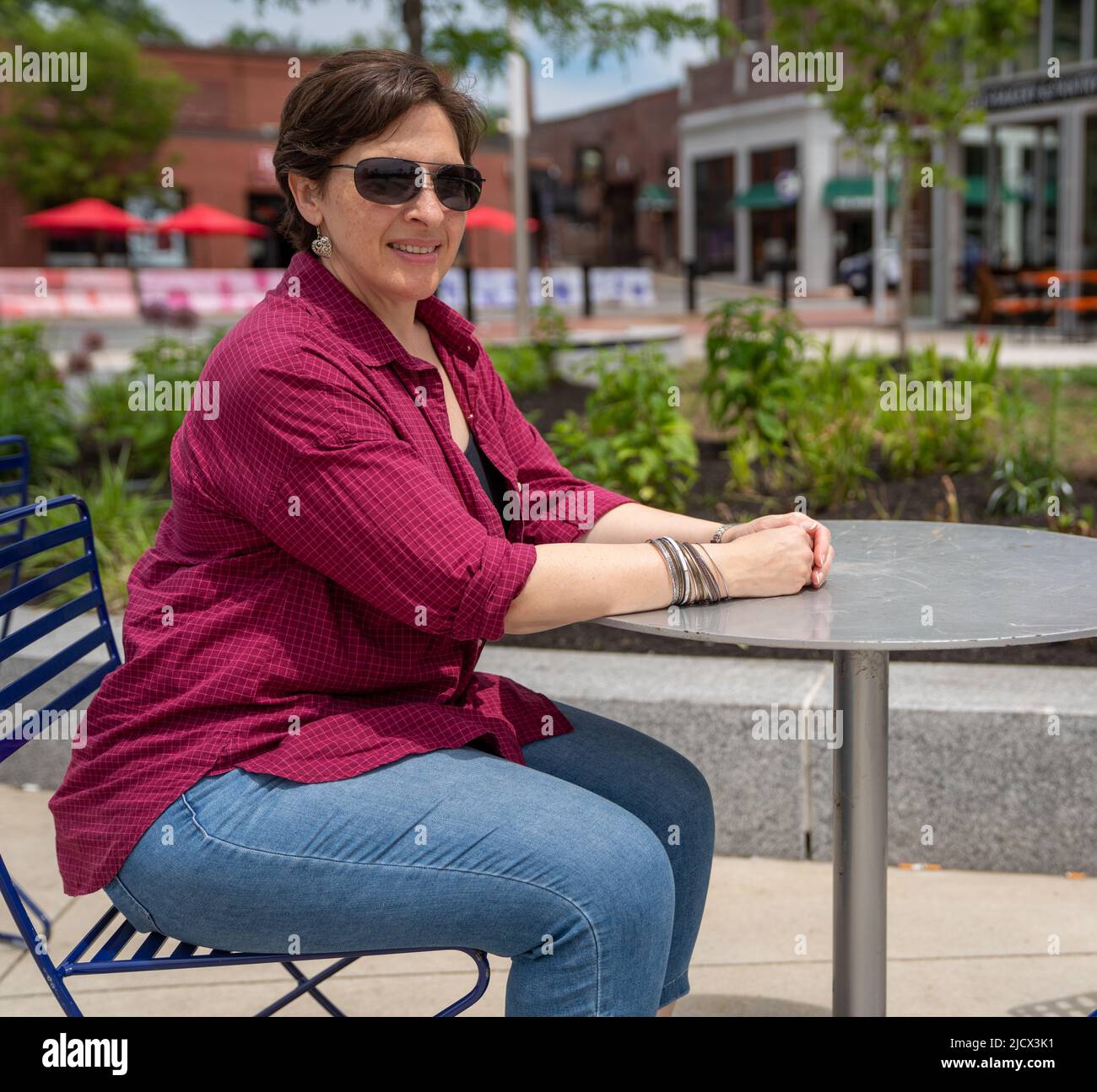 Felice, donna matura seduta ad un tavolo all'aperto da solo Foto Stock