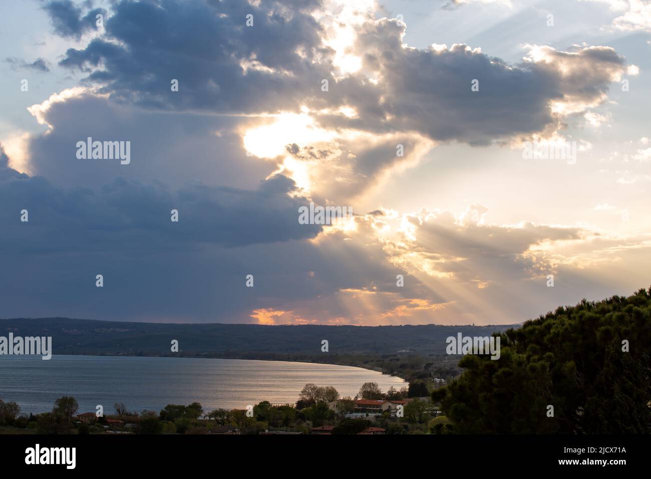 Cielo nuvoloso mistico e drammatico con il sole dietro le nuvole e raggi di luce sul lago. Foto in stile artistico Foto Stock